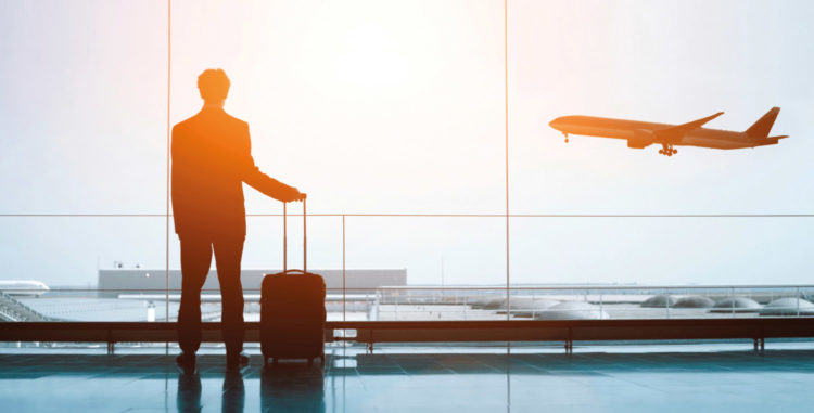 A person in a airport carrying a handbag looking at a plane depart through a window