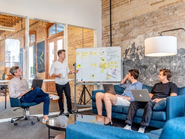 One person presenting to 3 other persons seating in sofas in the office with their laptops