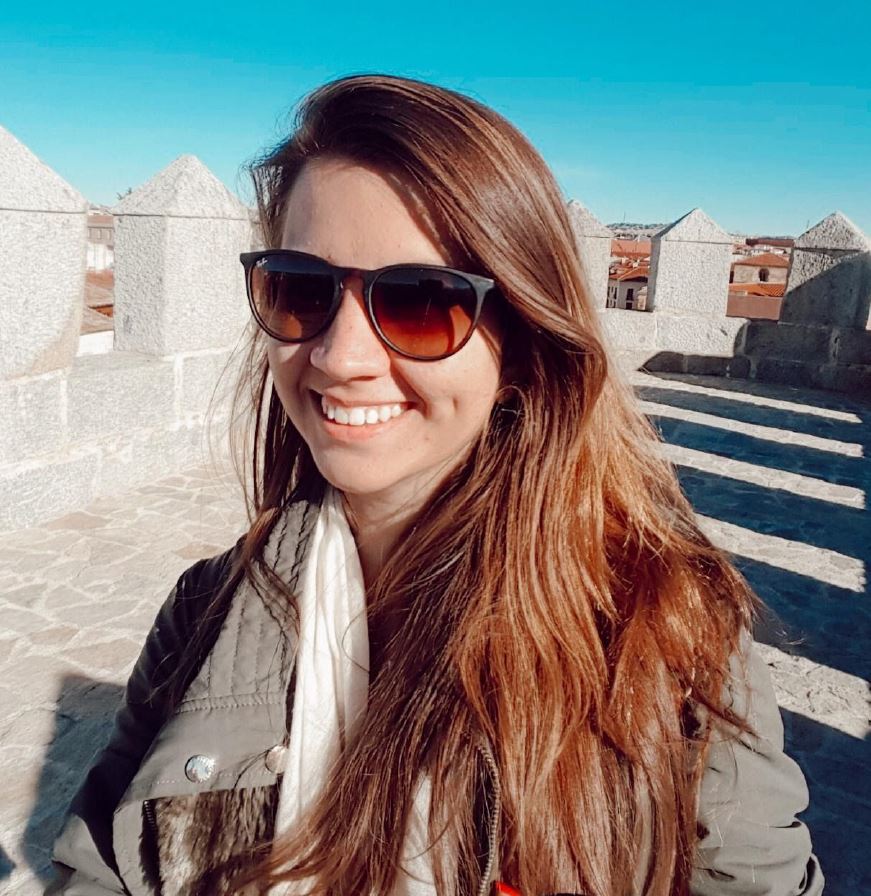 Gabriela smilling in the sun with sun glasses with what looks a terrace in a castle like building