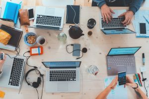 A table filled with laptops and different electronic gadgets and people working