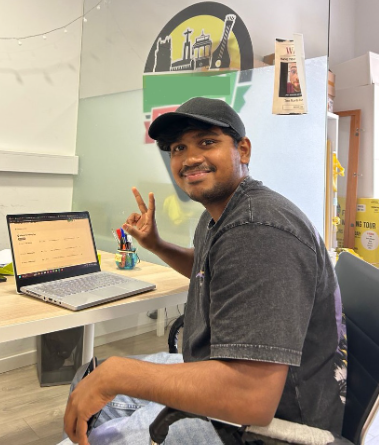 Rishi posing seated on the desk with laptop
